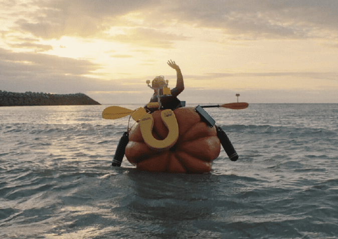 Persoon op een reusachtige pompoen als boot op zee bij zonsondergang, wuivend met een peddel