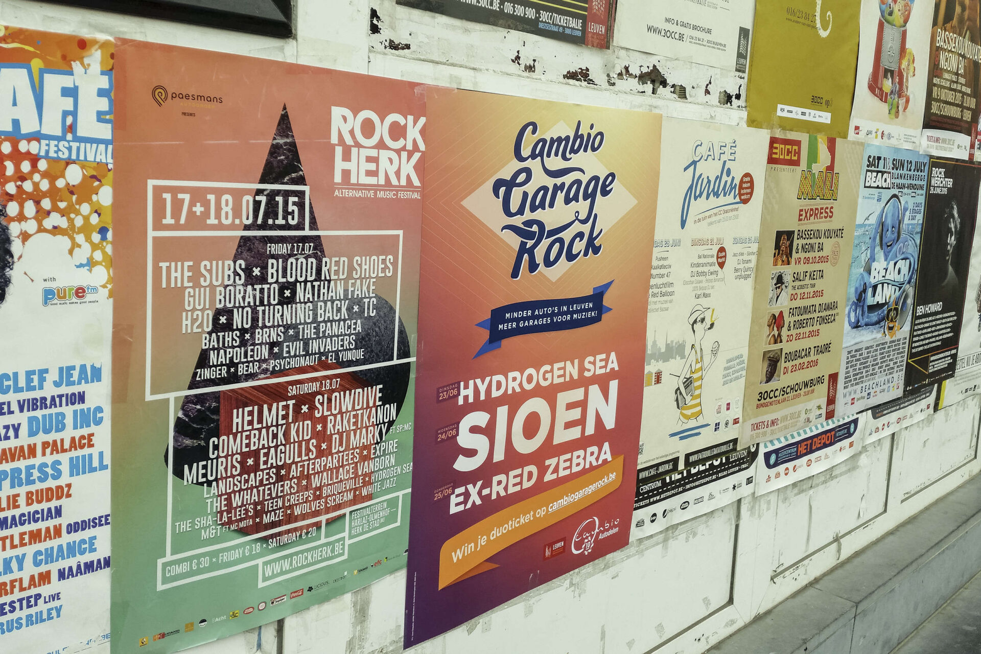Affichewand met Belgische evenementposters, waaronder Rock Herk festival en Cambio Garage Rock